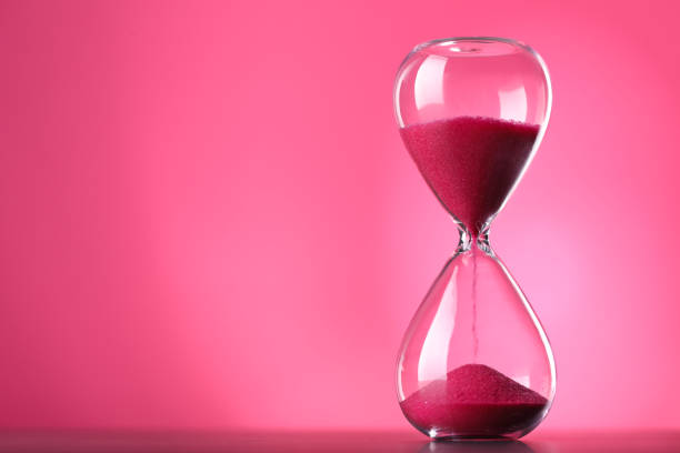 istock Hourglass with flowing sand on table against pink background, space for text 1875188551