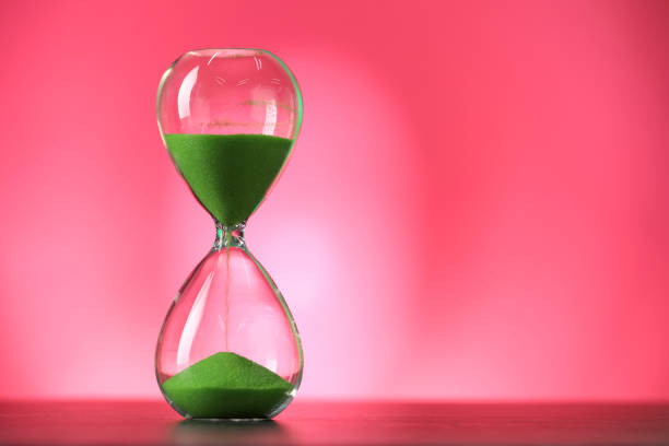 istock Hourglass with flowing green sand on table against pink background, space for text 1875190684