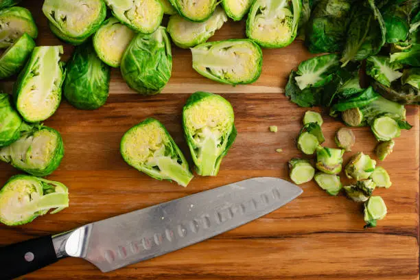Fresh brussels sprouts halved with a santoku knife on a wooden carving board