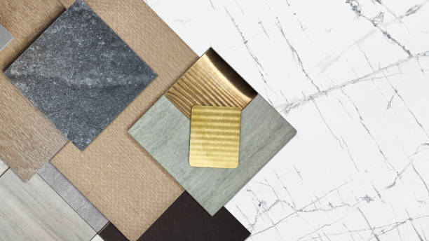 group of interior material samples including gold stainless, gold metallic aluminium, palette of stone tiles, wooden veneer, quartz, artificial stone placed on white marble table, close up view.