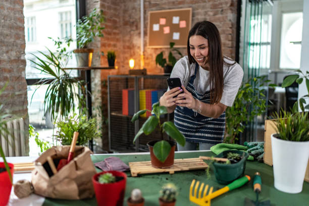istock Beautiful woman having video call while potting plants at home 1875215635