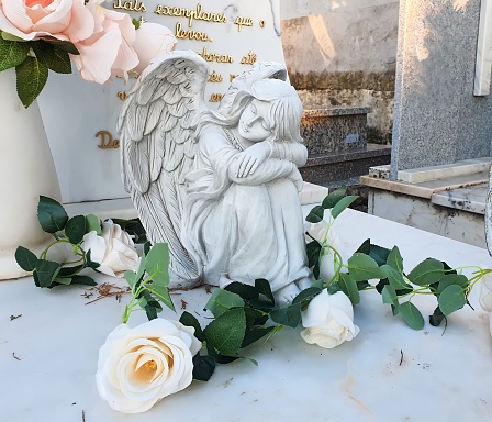 A white angelic figure on a gravestone in the cemetery, a poignant representation of enduring love as the departed's loved ones continue to express affection even beyond death.