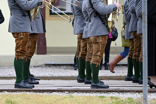 The legs of members of a brass band in leather pants and dirndls line up to perform a march