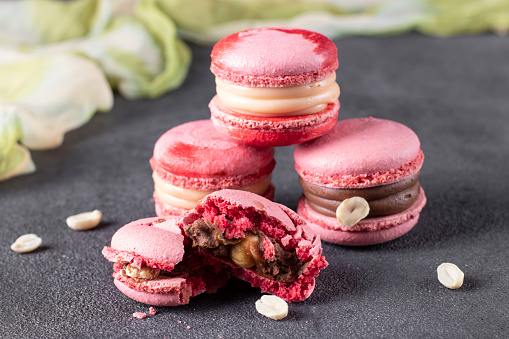 Pink macarons with hazelnuts and caramel on dark gray background