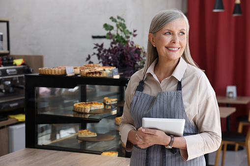 Happy business owner with tablet in her cafe, space for text
