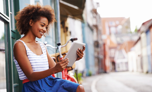 Young smiling woman sitting on a bench with her bicycle reading her digital tablet