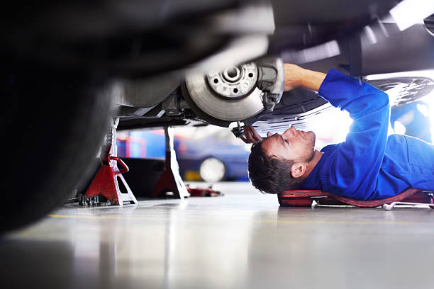 Making sure it's 100 percent road worthy A car mechanic working on the underside of a car auto repair shop stock pictures, royalty-free photos & images