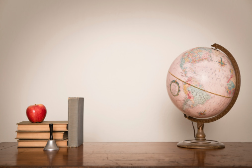 Color image of  vintage books, an apple, a bell, and a globe sitting on an antique, wood desk.  With room for your text.