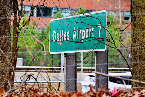 Reston, Virginia, USA - December 7, 2023: Mileage sign seen through a fence for Dulles Airport along the Dulles Toll Road in Northern Virginia.