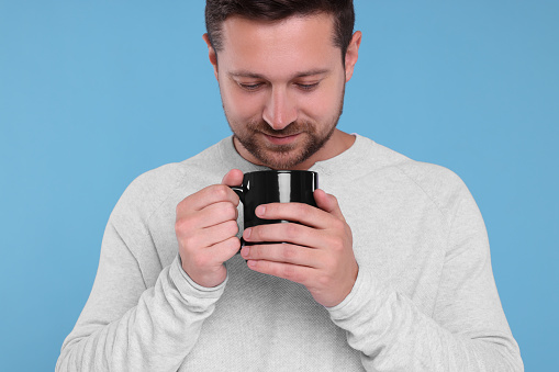 Man holding black mug on light blue background