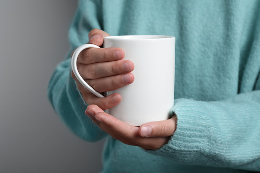 Woman holding white mug on gray background, closeup