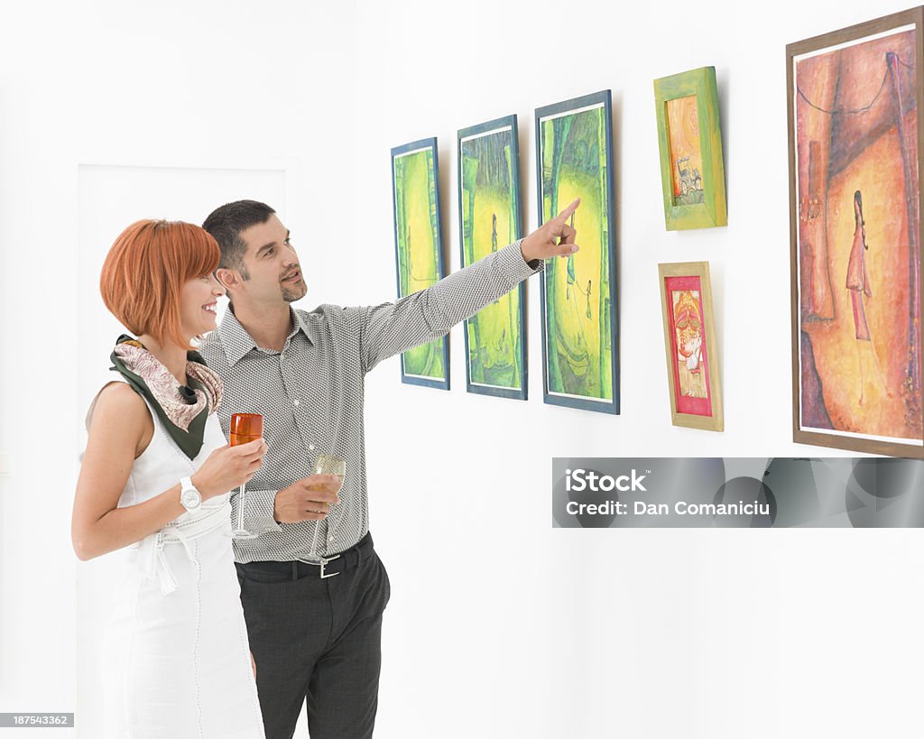 trying to understand an artwork handsome man standing in an art gallery next to a redhead attractive woman, pointing at some framed paintings Art Museum Stock Photo