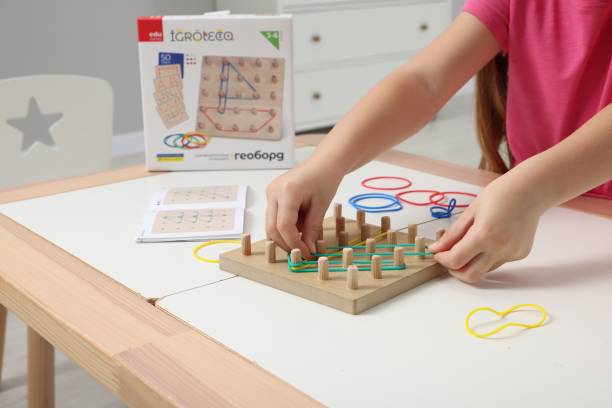 istock Motor skills development. Girl playing with geoboard and rubber bands at white table indoors, closeup 1875438575