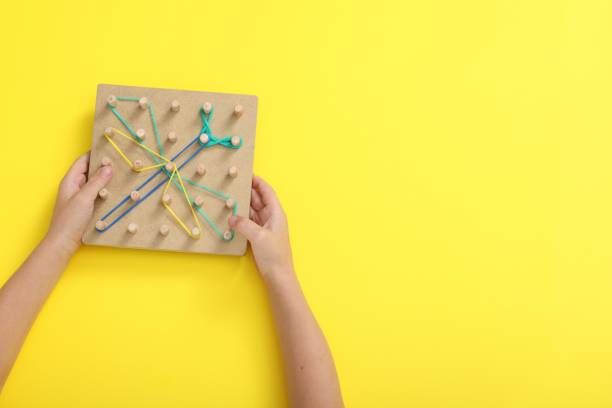 istock Motor skills development. Boy with geoboard and rubber bands at yellow table, top view. Space for text 1875438580