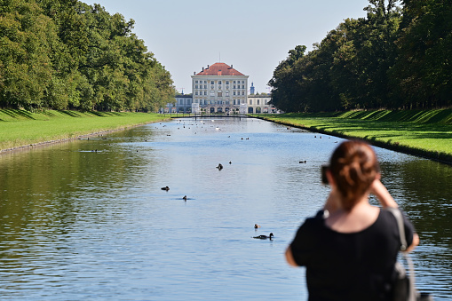 Woman taking a photo of the pond in front of the Nymphenburg Palace in the Bavarian capital Munich. It was the summer residence of the Electors and Kings of Bavaria from the House of Wittelsbach from 1715 to 1918.