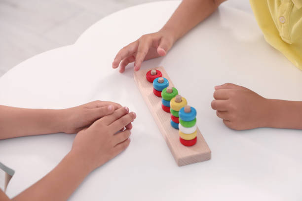 istock Little children playing with stacking and counting game at desk, closeup. Kindergarten activities for motor skills development 1875496817