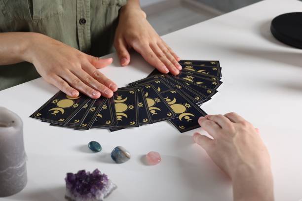 istock Astrologer predicting client's future with tarot cards at table indoors, closeup 1875497840