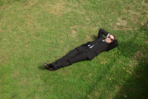 Businessman is resting on grass.
