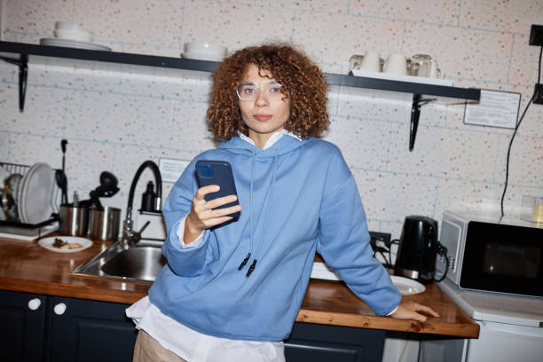 Girl Student in Kitchen Waist up portrait of curly haired young woman standing in kitchen and looking at camera with flash flash stock pictures, royalty-free photos & images