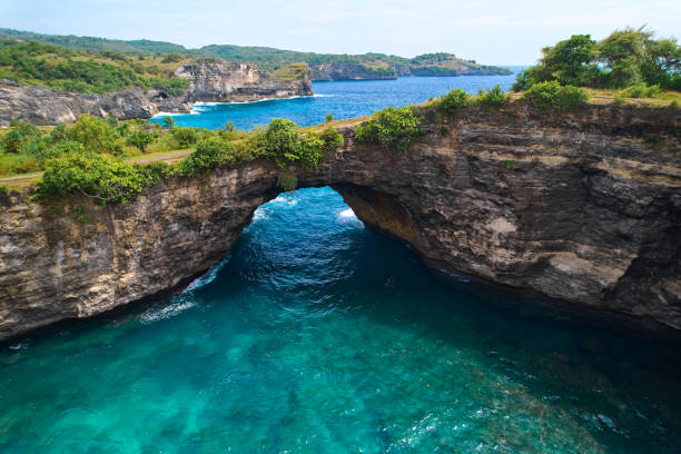 istock Rock broken by an ocean wave forming an arch in the mountain. Cliff is washed by powerful waves of ocean. Angel's Billabong is a popular tourist destination on the island of Nusa Penida in Indonesia. 1875519546