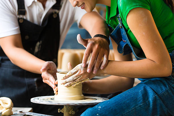 Potter creating clay bowl on turning wheel Female Potter creating a bowl on a Potters wheel, the master potter helping her homemade pottery wheel stock pictures, royalty-free photos & images