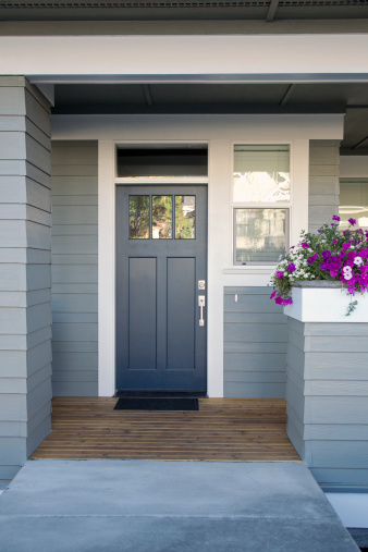 A gray front door of a home with front porch and flowers.