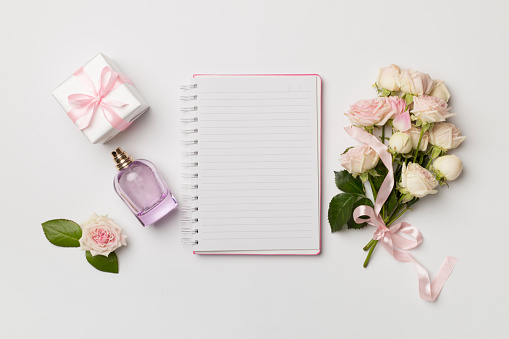 Notebook, gift box and rose flowers on white background, top view.