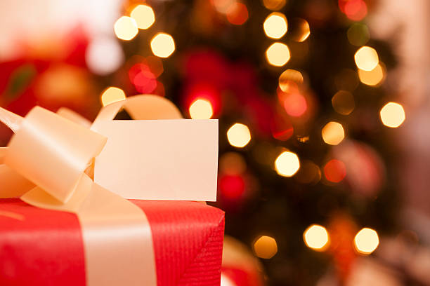 Christmas present with blank tag in front of a lighted tree.  Selective focus on the blank tag.