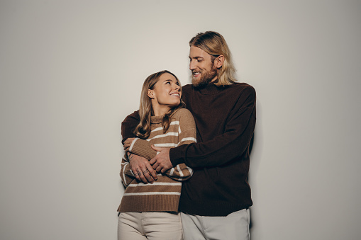 Fashionable young loving couple embracing and looking at each other with smiles on beige background