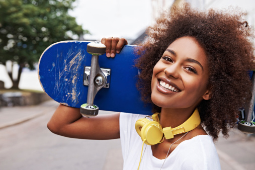 Young smiling woman with her skateboard on her shoulder