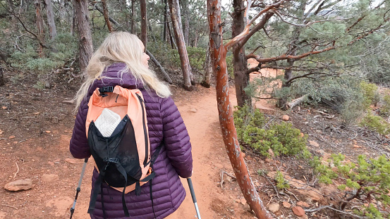 Mature woman hikes along red earth path through juniper forest