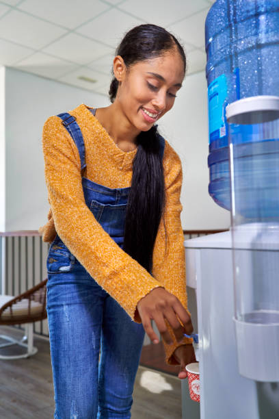 pretty Colombian Latin girl drinking water from the machine at the co working center taking a break