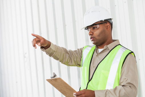 Hispanic man (30s) wearing hardhat and safety vest, giving orders.