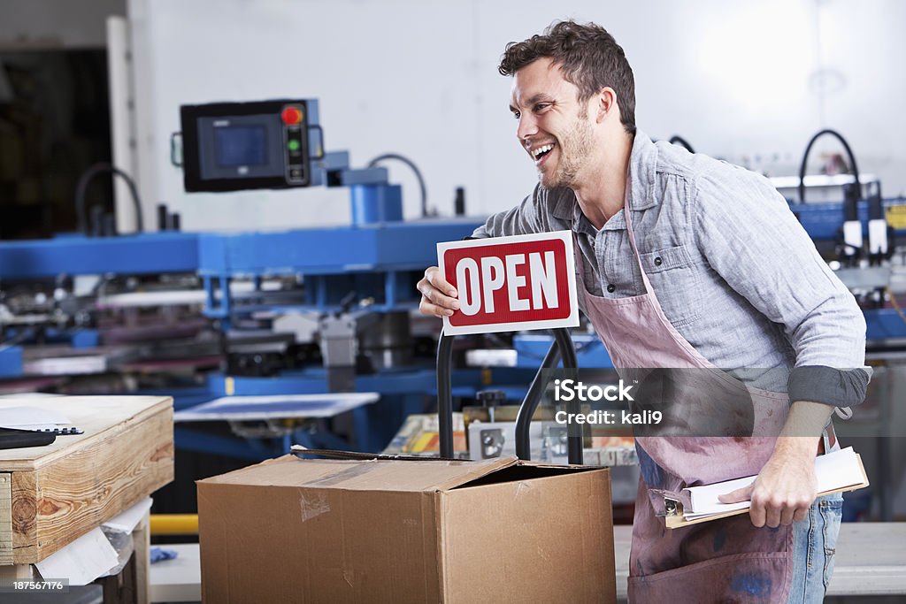 Man in screen printing business Small business - young man (20s) working in screen printing shop, holding OPEN sign. 20-29 Years Stock Photo