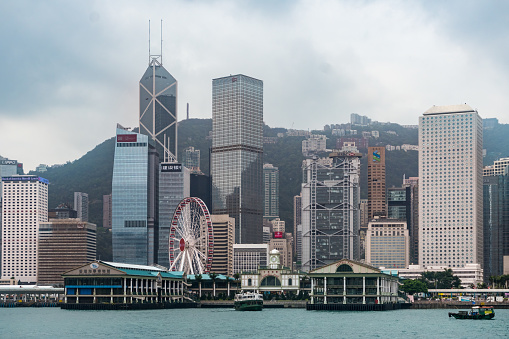 Hong Kong, China - May 1, 2018: Panorama of Hong Kong skyline downtown skyscrapers over Victoria Harbour in evening with junk tourist ferry boat on sunset and dramatic sky. Hong Kong, China