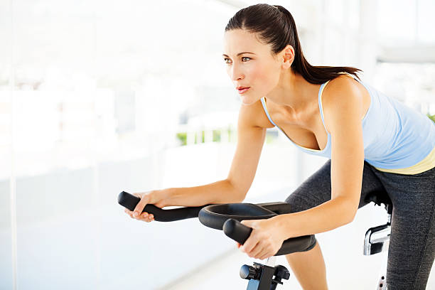 donna guardando lontano durante l'esercizio su bicicletta in palestra - spinning instructor exercising gym foto e immagini stock