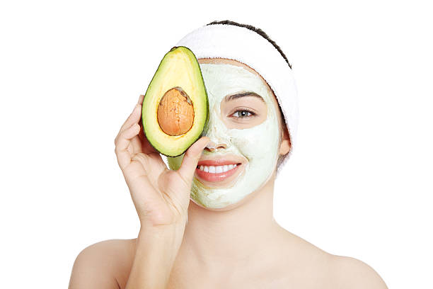 Pretty woman holding an avocado over her clay facial mask stock photo