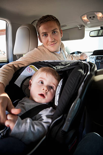 Father with baby in car seat Young father (20s) with baby boy (8 months) strapped in a car seat.  Focus on man. Sc0601 stock pictures, royalty-free photos & images