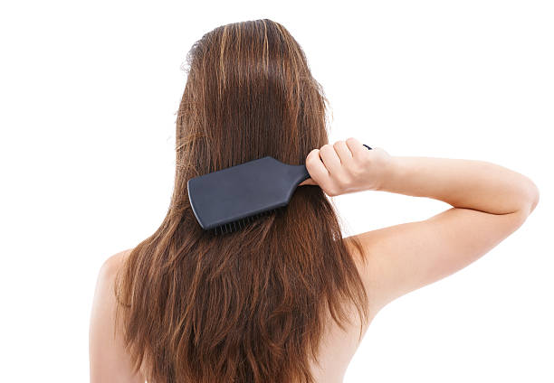 Rearview of a beautiful young woman brushing her hair while standing against a white backgrund