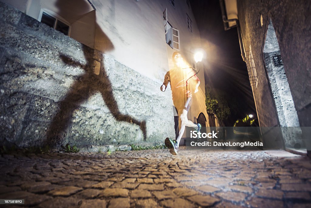 City Running at Night Young man running and training outdoors at night, casting a shadow on the walls of an old European city.   Ghost Stock Photo