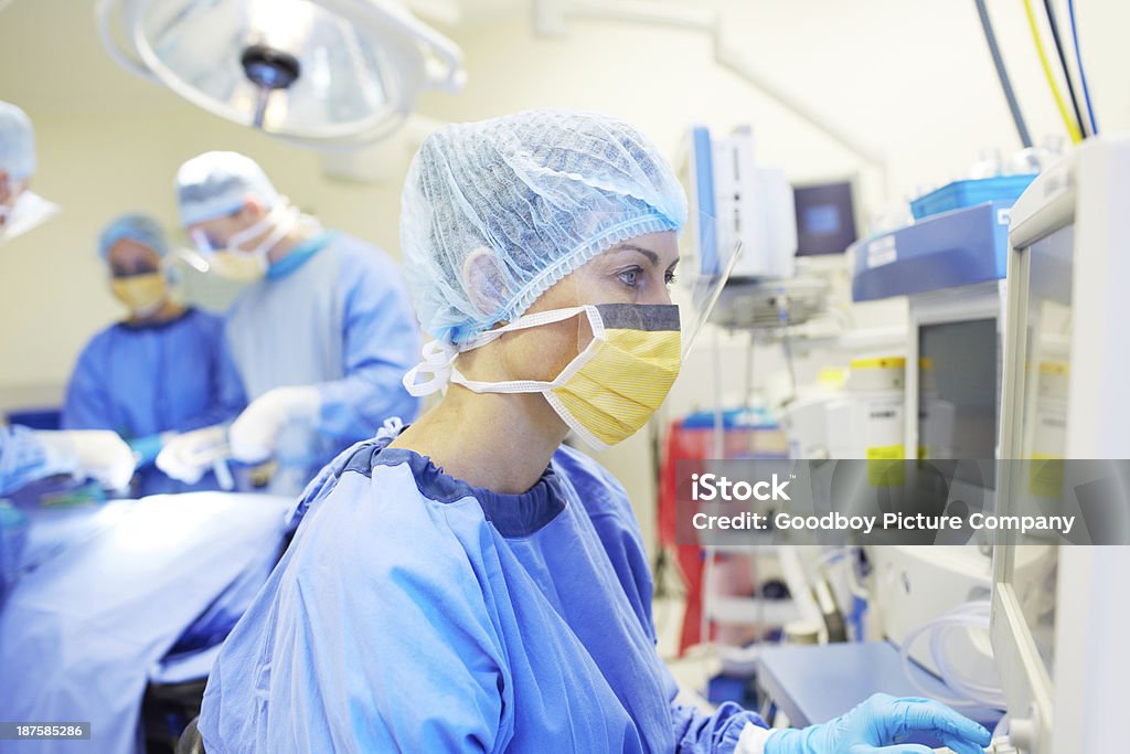 Monitoring their patient's vitals Surgical nurse monitoring a patient's vitals in an operating room Nurse Stock Photo