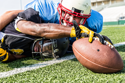 A football player reaches for the touchdown as he is tackled during a football game.