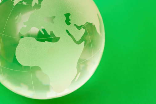 A glass globe-shaped paperweight on a green background with the African continent uppermost. Copy space on green. 