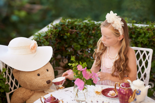 A little girl sitting outside having a tea party with her teddy bear