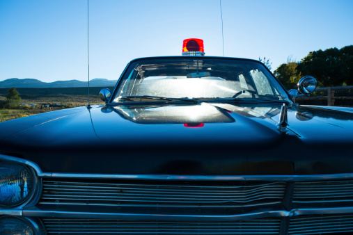 Vintage police car with red flashing light and blue skies on clear day with bright sun shining through windshield..