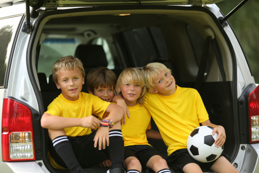 Portrait of happy young soccer players sitting in open car trunk