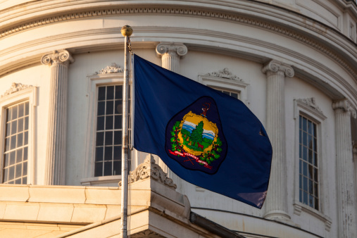 The state flag flies in front of the dome at the Vermont State House, Montpelier, VT.