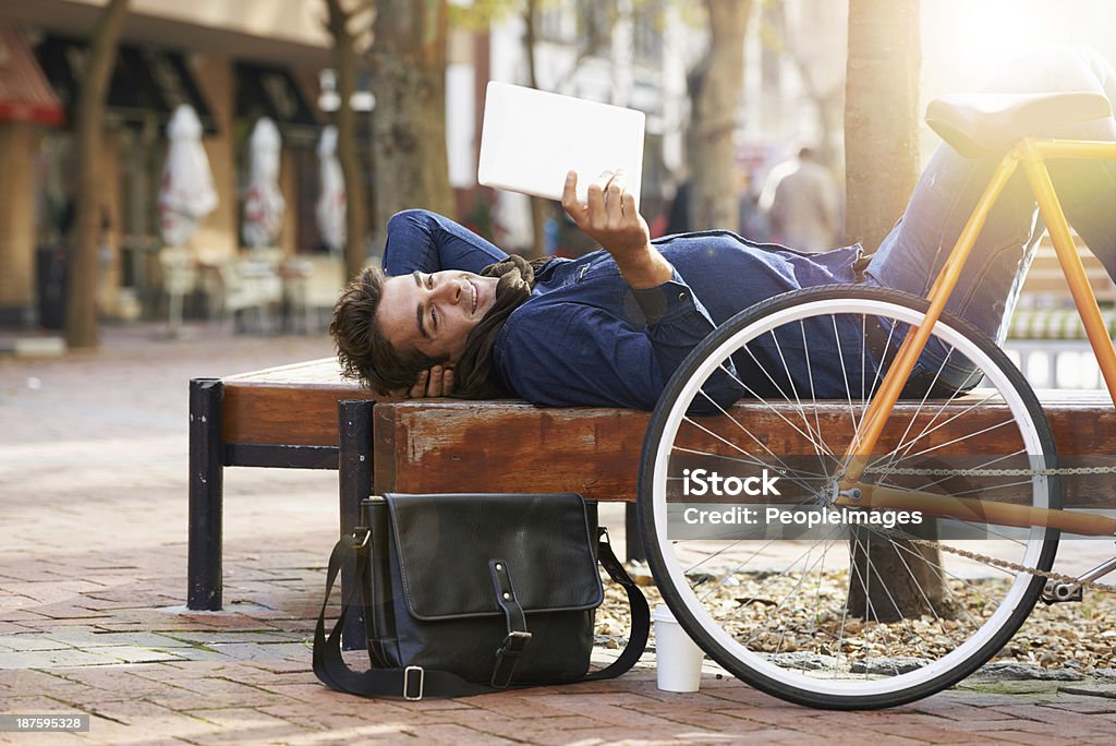 Make the city your home! Shot of a young man relaxing on a bench with his digital tablet while his bicycle stands next to him Lifestyles Stock Photo