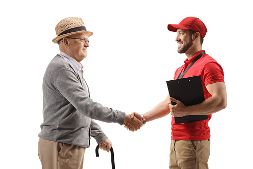 Profile shot of a delivery man shaking hands with a senior man with a cane isolated on white background