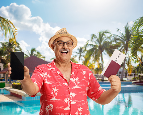 Mature male tourist holding a passport and a mobile phone by a swimming pool